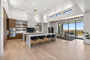 Kitchen with open shelves, an island with sink, modern cabinets, light wood-style flooring, and light stone countertops