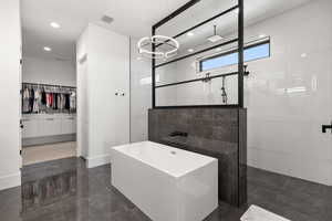 Full bath with a spacious closet, walk in shower, dark marble finish flooring, recessed lighting, and a freestanding tub