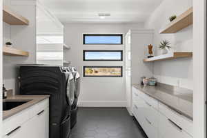 Washroom featuring dark tile patterned flooring, washer and clothes dryer, and cabinet space