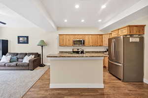 Kitchen featuring stainless steel appliances, recessed lighting, open floor plan, dark wood-type flooring, and a center island with sink