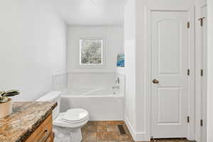 Bathroom featuring a bath, vanity, dark stone finish flooring, and a closet