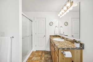 Full bathroom featuring vanity, a shower stall, and stone finish floors