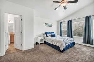 Bedroom with vaulted ceiling, light colored carpet, a ceiling fan, and ensuite bathroom