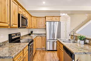 Kitchen with stainless steel appliances, light wood-type flooring, an island with sink, recessed lighting, and light stone counters