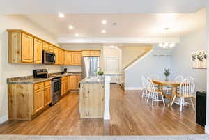 Kitchen featuring stainless steel appliances, decorative light fixtures, recessed lighting, dark stone countertops, and an island with sink