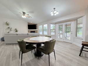 Dining space featuring lofted ceiling, light wood-style floors, a brick fireplace, ceiling fan, and a chandelier