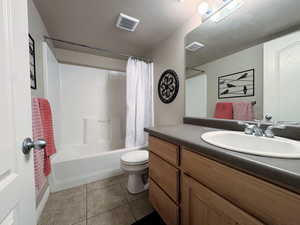 Bathroom featuring a textured ceiling, vanity, shower / bath combination with curtain, and dark tile patterned floors