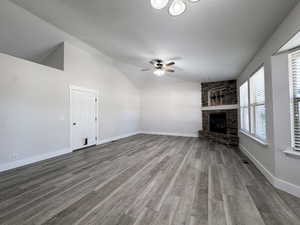 Unfurnished living room featuring light wood-style floors, lofted ceiling, a stone fireplace, and a ceiling fan