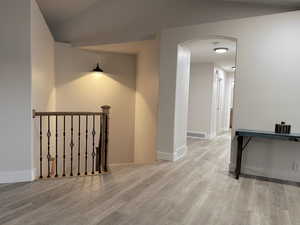 Hallway with arched walkways, light wood-style flooring, and an upstairs landing