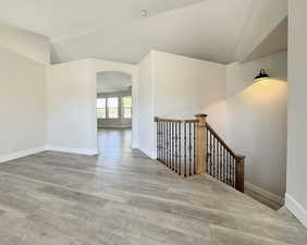 Unfurnished room with arched walkways, light wood-type flooring, and lofted ceiling