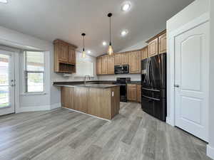 Kitchen with dark countertops, black appliances, lofted ceiling, hanging light fixtures, and a peninsula