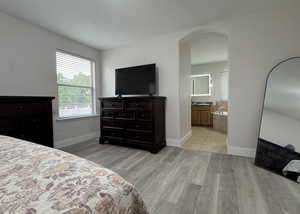 Primary Bedroom featuring arched walkways, light wood-style floors, and en-suite bath