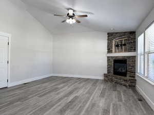 Unfurnished living room with vaulted ceiling, light wood-type flooring, a ceiling fan, and a fireplace