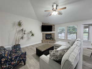 Living area with vaulted ceiling, light wood finished floors, a stone fireplace, and a ceiling fan
