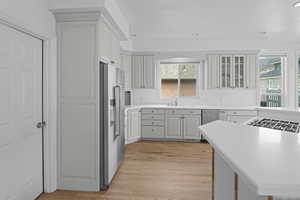 Kitchen featuring light countertops, stainless steel appliances, glass insert cabinets, light wood-type flooring, and recessed lighting