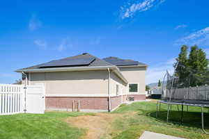 View of property exterior with a trampoline, brick siding, stucco siding, and roof mounted solar panels