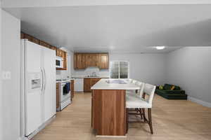 Kitchen featuring brown cabinets, light countertops, white appliances, a breakfast bar, and light wood-style flooring
