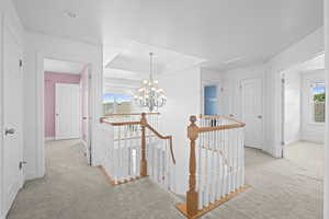 Hall featuring an upstairs landing, light colored carpet, and plenty of natural light