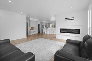 Living area with recessed lighting, light wood-style floors, and a glass covered fireplace