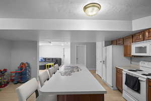 Kitchen with white appliances, brown cabinets, a kitchen breakfast bar, light wood-style floors, and light countertops