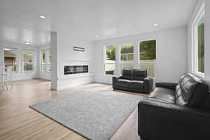 Living area featuring healthy amount of natural light, light wood finished floors, a glass covered fireplace, and recessed lighting