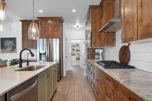 Kitchen with quartz and granite counters, decorative light fixtures, appliances with stainless steel finishes, light woods-style floors, and recessed lighting