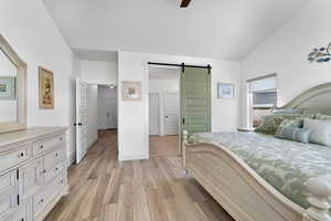 Bedroom featuring a barn door, light wood-style flooring, lofted ceiling, and a ceiling fan