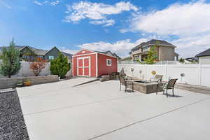 Fenced backyard featuring a fire pit, a storage unit with power, a patio area, and a residential view