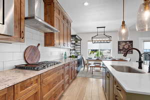 Kitchen with wood shaker cabinets, light quartz counters, backsplash, stainless steel hood, and decorative light fixtures