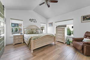 Bedroom featuring light wood-style flooring, a barn door, lofted ceiling, and a ceiling fan