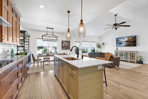 Kitchen featuring a center island with sink, light wood-style flooring, light quartz countertops, and lofted ceiling