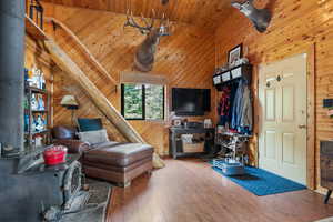 Living area featuring a wood stove, wood finished floors, wood walls, high vaulted ceiling, and wooden ceiling