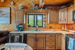 Kitchen featuring light countertops, a wooden ceiling with exposed beams, brown cabinetry, wood walls, and black appliances