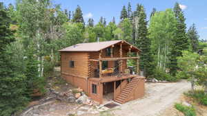 View of front of home with stairs, log siding, a wooden deck, and a wooded view