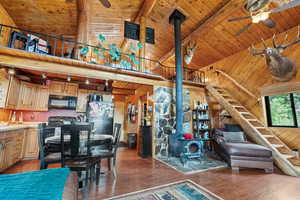 Living area featuring a wood stove, wood walls, ceiling fan, dark wood-style flooring, and a wooden ceiling with exposed beams
