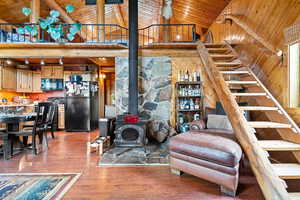Living area featuring stairs, a wood stove, a wooden ceiling with exposed beams, light wood-style floors, and high vaulted ceiling