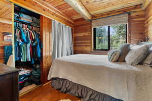 Bedroom featuring wood walls, a wood ceiling with exposed beams, wood finished floors, and a closet