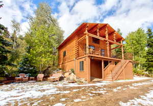 View of snow covered exterior with stairs, log exterior, a balcony, and a patio