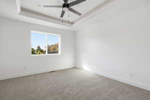 Unfurnished room with a raised ceiling, carpet flooring, and ceiling fan