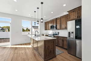Kitchen featuring appliances with stainless steel finishes, recessed lighting, light wood-type flooring, hanging light fixtures, and dark brown cabinetry