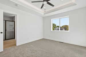 Unfurnished bedroom with a raised ceiling, ornamental molding, light colored carpet, a ceiling fan, and ensuite bathroom