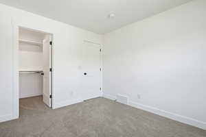 Unfurnished bedroom with light colored carpet and a walk in closet