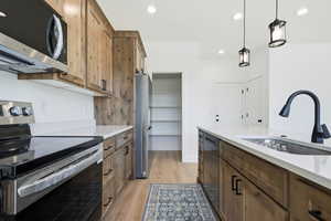 Kitchen with appliances with stainless steel finishes, light wood-style flooring, decorative light fixtures, recessed lighting, and light stone countertops
