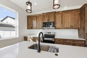 Kitchen with appliances with stainless steel finishes, brown cabinetry, recessed lighting, hanging light fixtures, and light stone counters