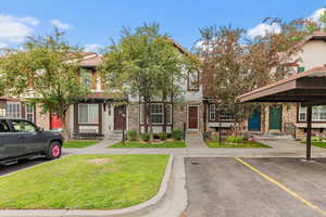 View of front of house featuring stone siding, covered and uncovered parking, and a front lawn