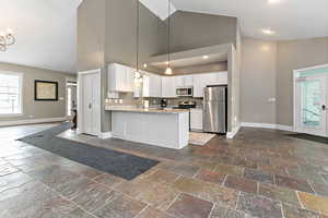Kitchen with white cabinets, decorative light fixtures, stainless steel appliances, stone tile floors, and high vaulted ceiling