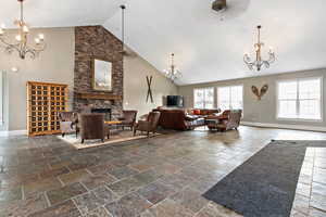 Living area featuring a chandelier, high vaulted ceiling, stone tile floors, and a stone fireplace