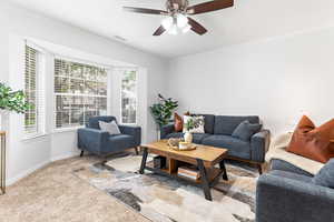 Living area featuring light colored carpet, ornamental molding, and a ceiling fan