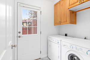 Laundry area featuring light tile patterned floors, cabinet space, and washer and dryer