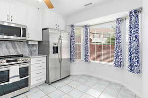 Kitchen with stainless steel appliances, white cabinetry, light tile patterned floors, and backsplash